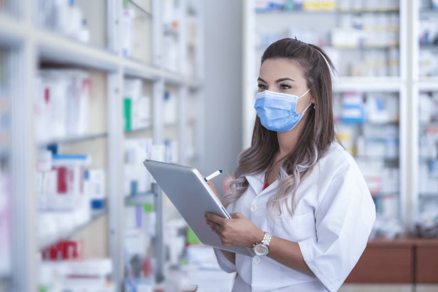 Pharmacy technician in face mask taking stock of inventory