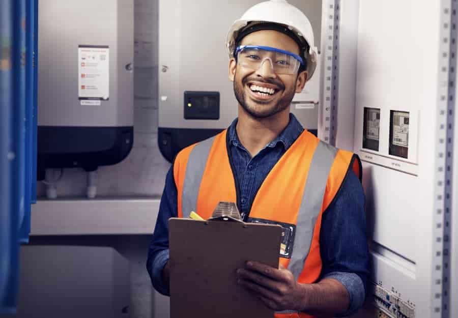 Smiling electrician with clipboard at control panel
