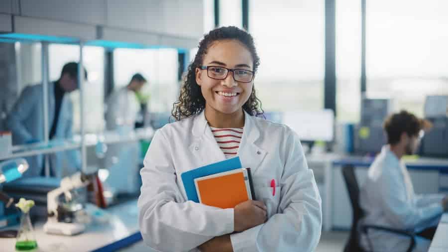 Medical assistant student wearing white coat and holding books