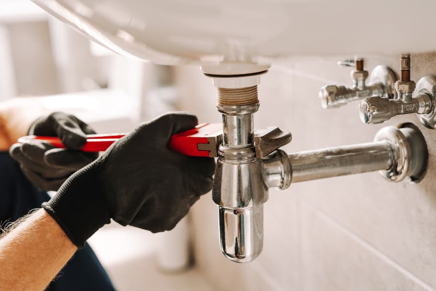 Plumber in black gloves fixes sink pipe with a wrench in bathroom