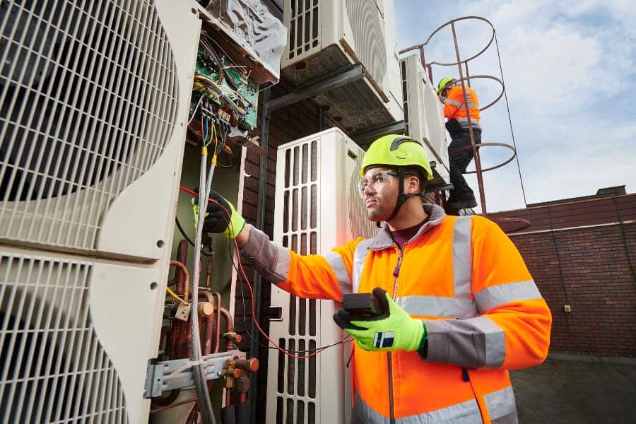 Maintenance engineers servicing air conditioning units on rooftop of commercial building