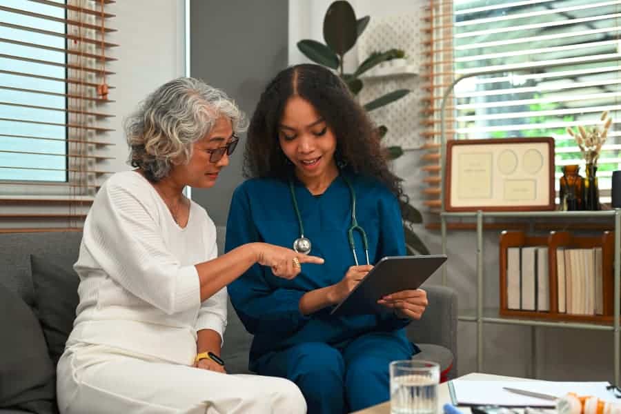 Medical assistant in blue scrubs with tablet talking to patient