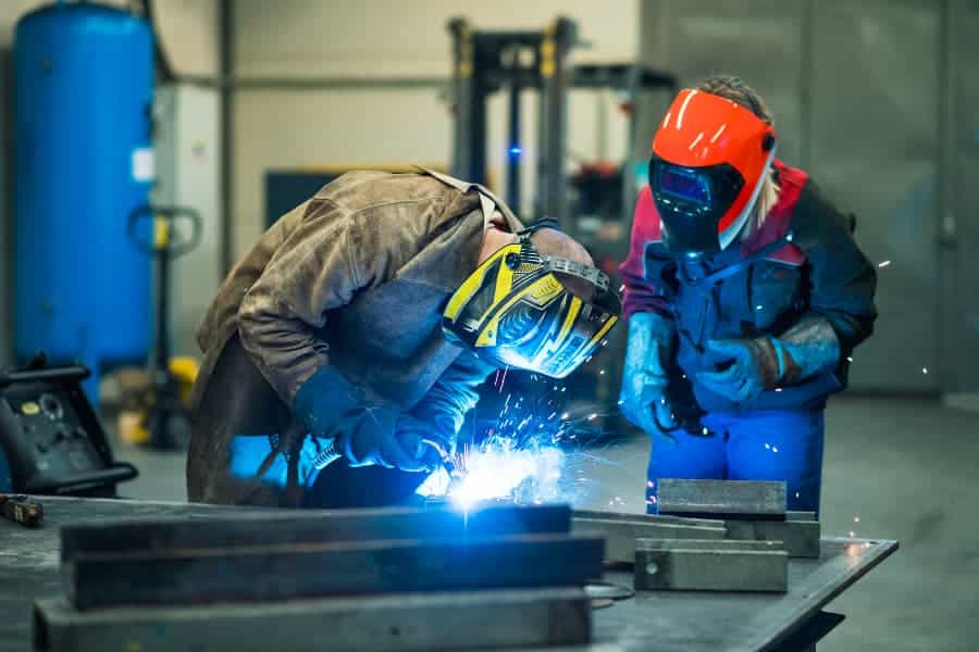 Welder in yellow helmet working near welder in orange helmet